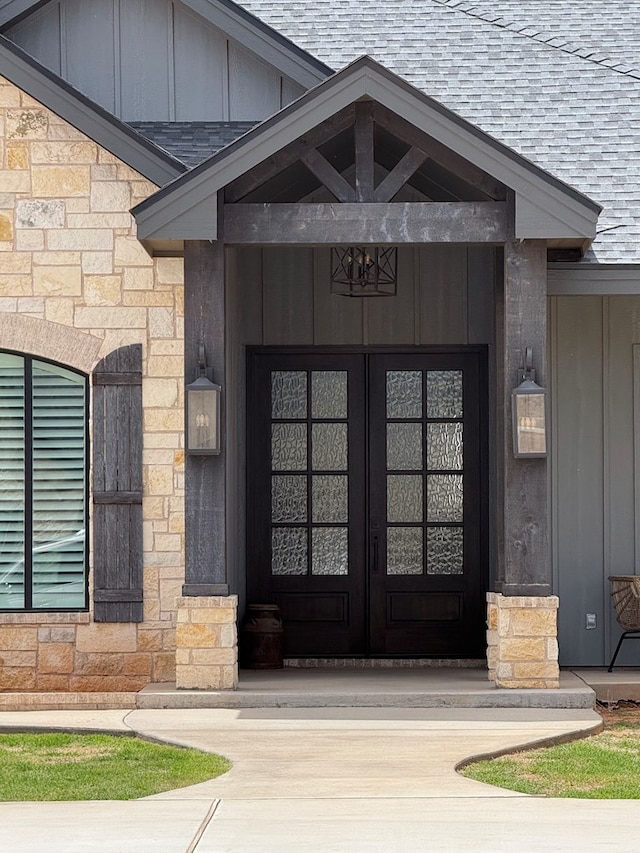 view of exterior entry featuring a shingled roof, stone siding, and board and batten siding