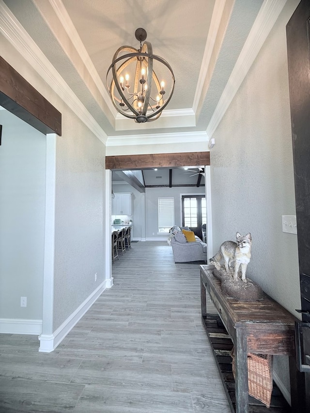 corridor with wood finished floors, crown molding, an inviting chandelier, a textured wall, and a raised ceiling