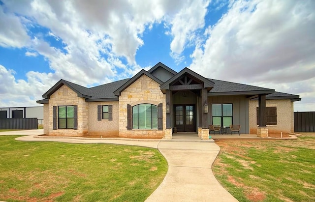 view of front facade featuring stone siding, board and batten siding, french doors, and a front yard