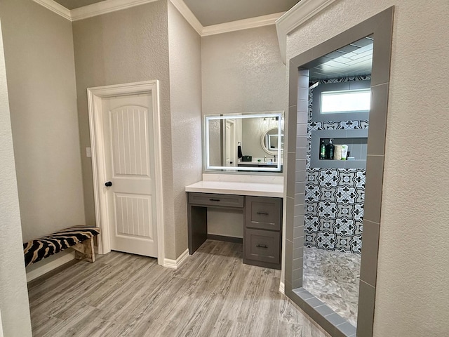 bathroom featuring wood finished floors, tiled shower, ornamental molding, and a textured wall