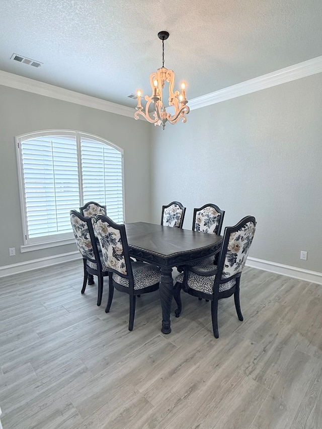 dining room with a textured ceiling, ornamental molding, light wood-type flooring, visible vents, and a chandelier