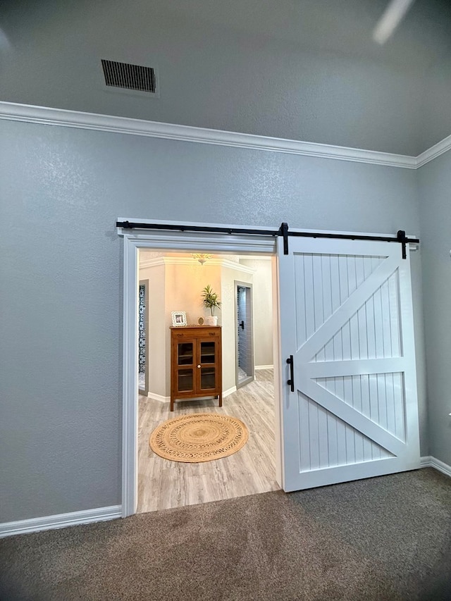 interior space with a barn door, baseboards, ornamental molding, visible vents, and wood finished floors