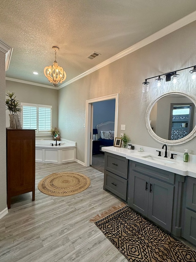 ensuite bathroom featuring a textured ceiling, vanity, a chandelier, crown molding, and wood finished floors