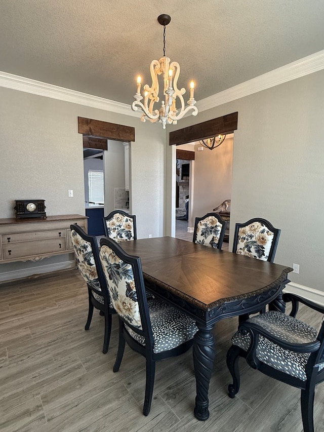dining space with ornamental molding, a notable chandelier, light wood-type flooring, and a textured ceiling