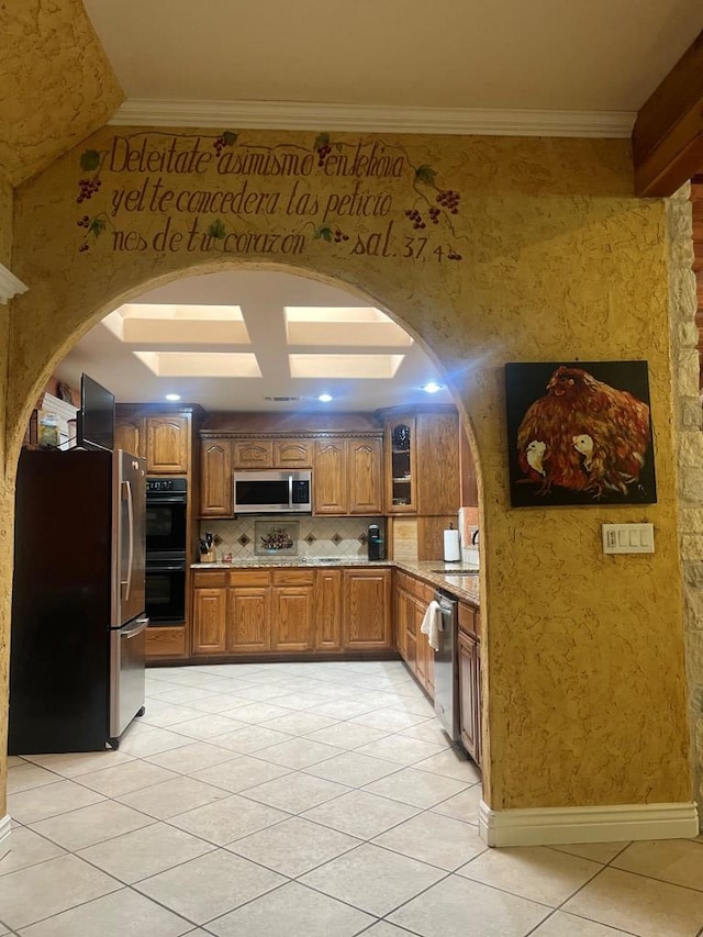 3934 N Bucknell Ave, Odessa, TX 79764 - kitchen featuring stainless steel appliances, arched walkways, brown cabinets, light tile patterned floors, and backsplash