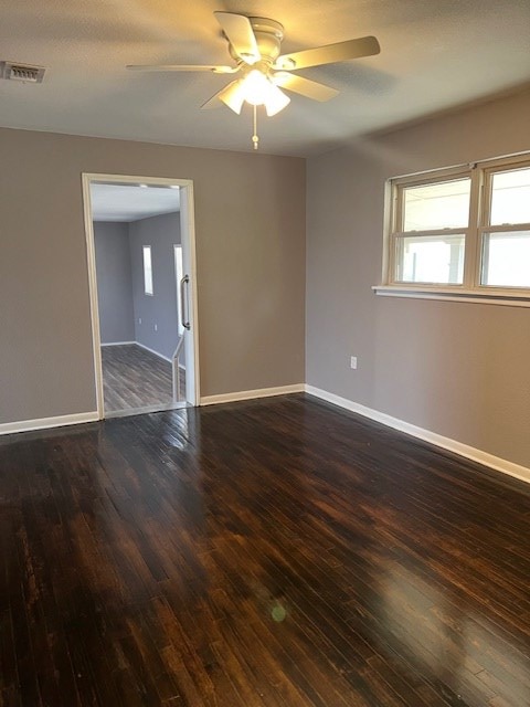 empty room with ceiling fan, visible vents, dark wood-style floors, and baseboards