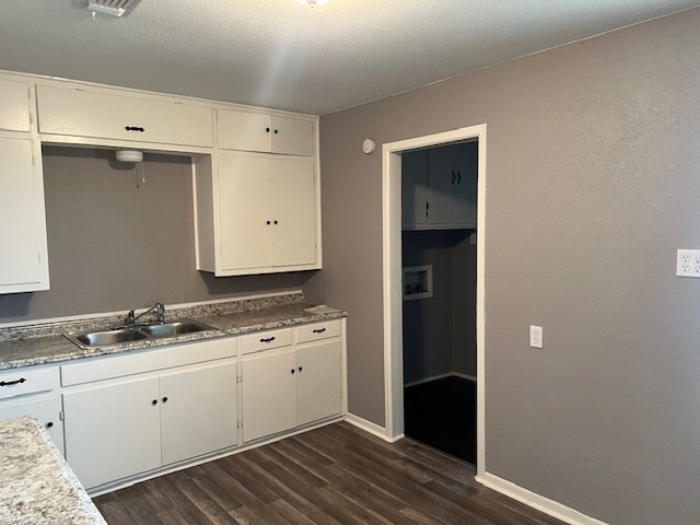 kitchen with baseboards, a sink, dark wood-style flooring, and white cabinetry