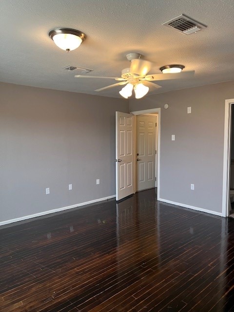 empty room featuring baseboards, dark wood-type flooring, and visible vents