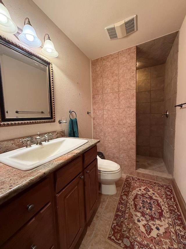 bathroom with toilet, tiled shower, and vanity