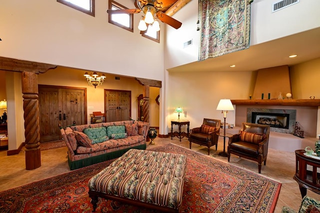 living room featuring light tile patterned floors, a large fireplace, ceiling fan with notable chandelier, and a high ceiling