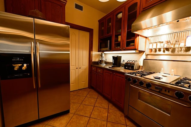 kitchen featuring light tile patterned flooring, dark stone countertops, stainless steel appliances, and range hood