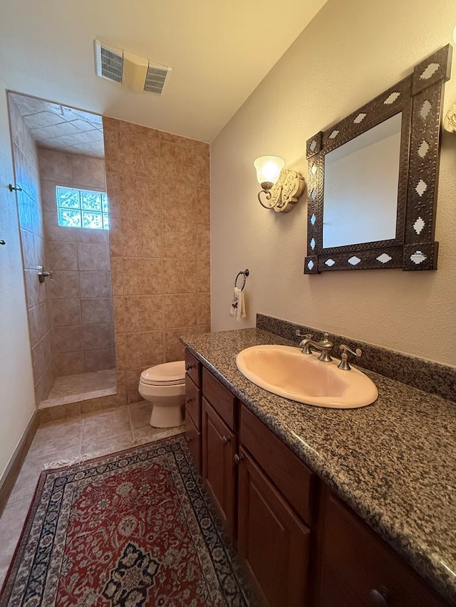 bathroom featuring toilet, tile patterned floors, vanity, and tiled shower