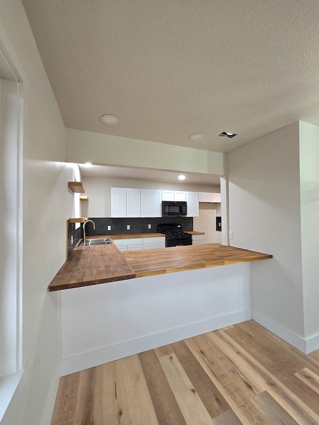 2500 Roper St, Odessa, TX 79761 - kitchen featuring butcher block countertops, black appliances, a peninsula, light wood-style flooring, and white cabinetry