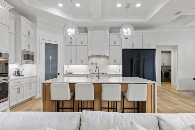 kitchen featuring decorative light fixtures, built in appliances, premium range hood, and an island with sink