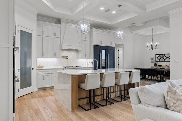 kitchen featuring white cabinets, premium range hood, a kitchen island with sink, and built in fridge