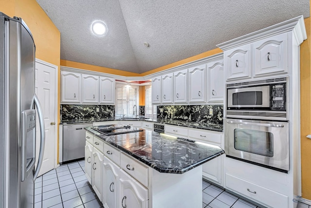 6415 San Mateo Ln, Odessa, TX 79762 - kitchen featuring appliances with stainless steel finishes, light tile patterned floors, vaulted ceiling, a center island, and white cabinets