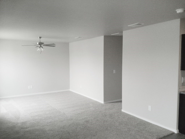 carpeted spare room featuring baseboards, ceiling fan, and visible vents