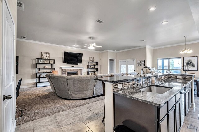 811 E 97th Ct, Odessa, TX 79765 - kitchen with a sink, a center island with sink, a ceiling fan, a fireplace, and dark stone countertops