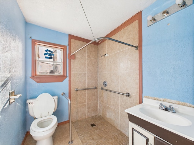 bathroom with a tile shower, a textured wall, toilet, vanity, and baseboards