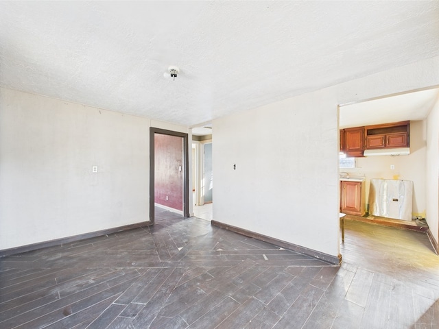 unfurnished living room with dark wood-style flooring, baseboards, and a textured ceiling