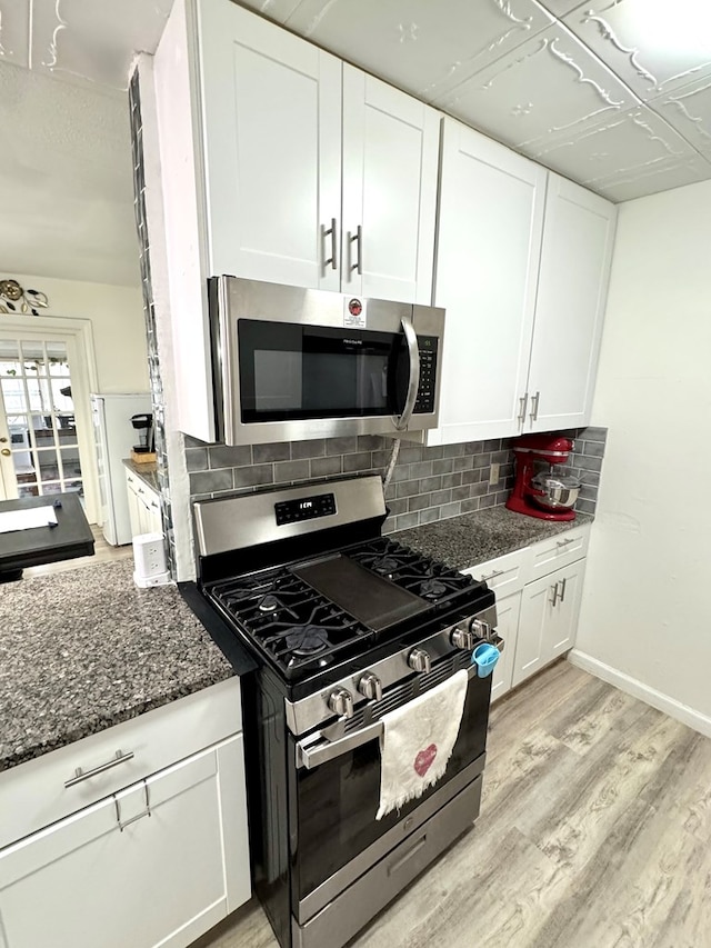 503 E Hendryx Ave, Alpine, TX 79830 - kitchen featuring appliances with stainless steel finishes, white cabinetry, light wood-style flooring, tasteful backsplash, and dark stone counters
