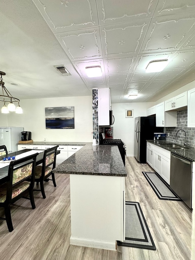 503 E Hendryx Ave, Alpine, TX 79830 - kitchen with stainless steel appliances, a peninsula, white cabinets, light wood finished floors, and a sink