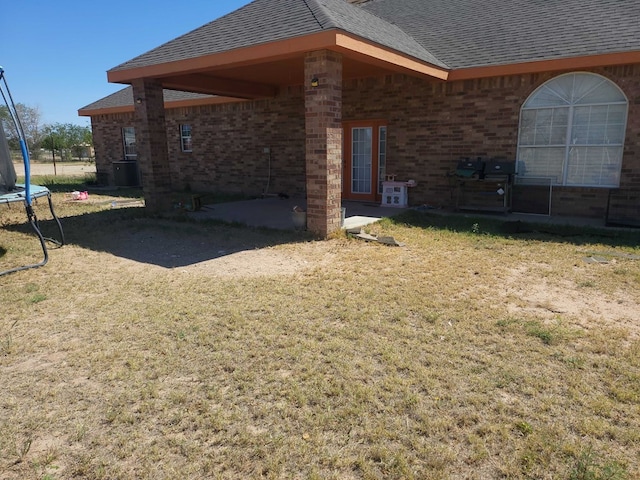 back of property with a yard, a trampoline, a shingled roof, and brick siding