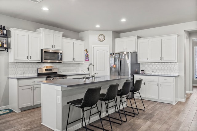 3102 Mearns Ct, Midland, TX 79705 - kitchen with stainless steel appliances, light wood-type flooring, a kitchen breakfast bar, decorative backsplash, and a center island with sink