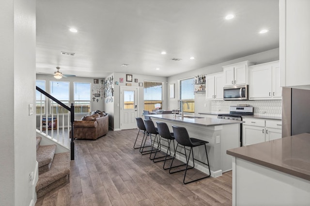 3102 Mearns Ct, Midland, TX 79705 - kitchen with appliances with stainless steel finishes, wood finished floors, an island with sink, tasteful backsplash, and white cabinetry