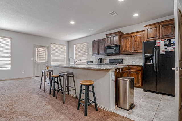 1506 San Miguel Ct, Midland, TX 79705 - kitchen featuring black appliances, a kitchen breakfast bar, an island with sink, backsplash, and light stone countertops