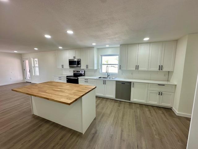 kitchen with appliances with stainless steel finishes, sink, white cabinets, a kitchen island, and butcher block counters