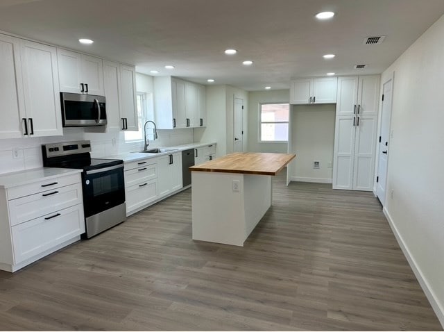 kitchen featuring butcher block counters, a center island, sink, stainless steel appliances, and white cabinets