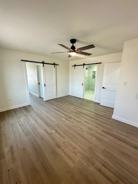 unfurnished bedroom featuring hardwood / wood-style floors, ceiling fan, a barn door, and connected bathroom