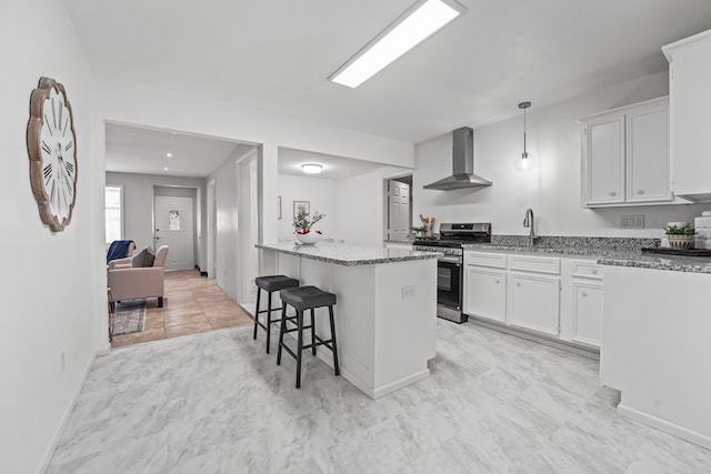 kitchen featuring stainless steel range with gas stovetop, wall chimney exhaust hood, light stone counters, a kitchen breakfast bar, and white cabinetry