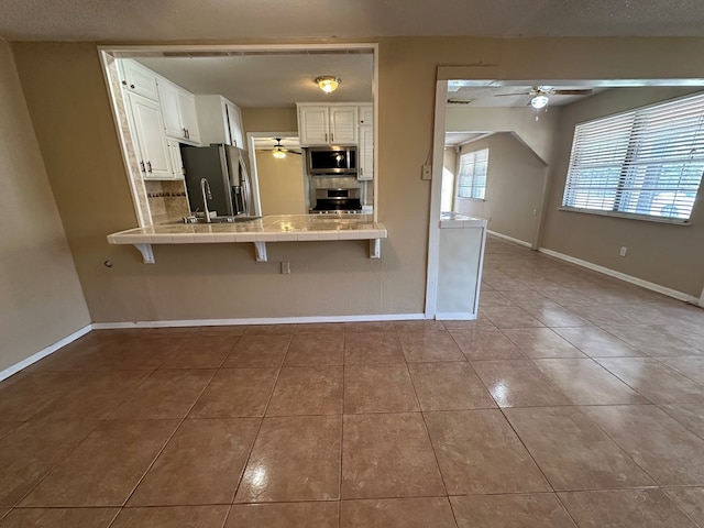 902 W 39th St, Odessa, TX 79764 - kitchen with stainless steel appliances, ceiling fan, tile counters, tile patterned floors, and white cabinets