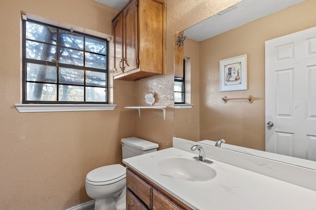 half bath with toilet, a textured wall, and vanity