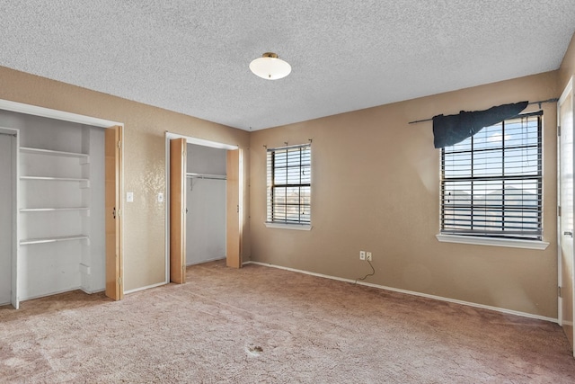 unfurnished bedroom with a textured ceiling, a textured wall, light colored carpet, baseboards, and two closets