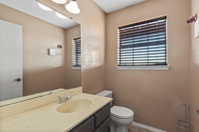 bathroom with toilet, a textured wall, vanity, and a healthy amount of sunlight