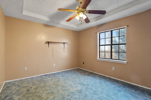 carpeted empty room featuring a textured ceiling, a raised ceiling, a ceiling fan, and baseboards