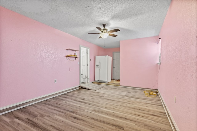 empty room featuring a textured ceiling, a textured wall, a ceiling fan, baseboards, and light wood-style floors