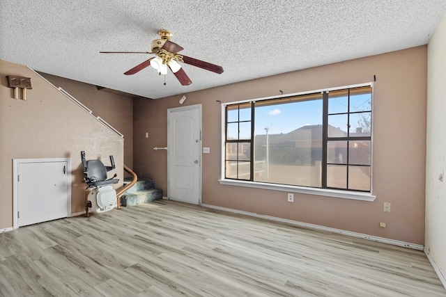 empty room with light wood-type flooring, baseboards, and a textured ceiling