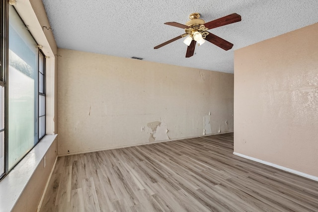 spare room featuring a textured ceiling, light wood-style flooring, visible vents, and a ceiling fan