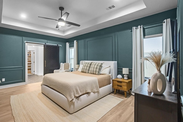 bedroom with light wood-style floors, a tray ceiling, a barn door, and visible vents