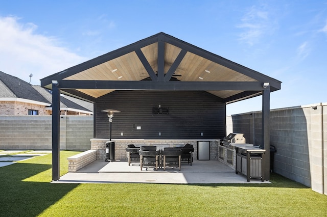 view of patio featuring exterior kitchen, a ceiling fan, and a fenced backyard