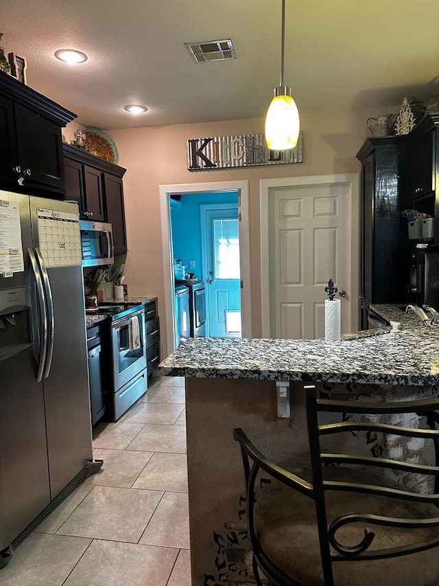kitchen with stainless steel appliances, separate washer and dryer, a kitchen bar, hanging light fixtures, and dark stone countertops