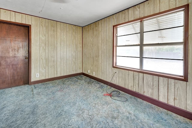 empty room with healthy amount of natural light, carpet floors, and wood walls