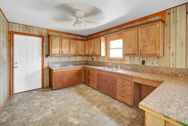 kitchen featuring a sink, a ceiling fan, light countertops, brown cabinets, and wooden walls