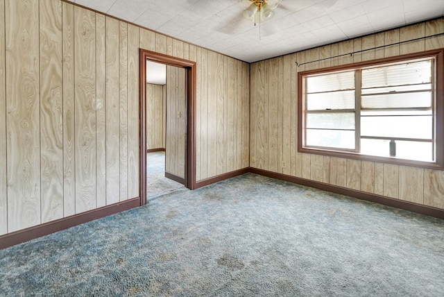 carpeted empty room with a ceiling fan and wooden walls