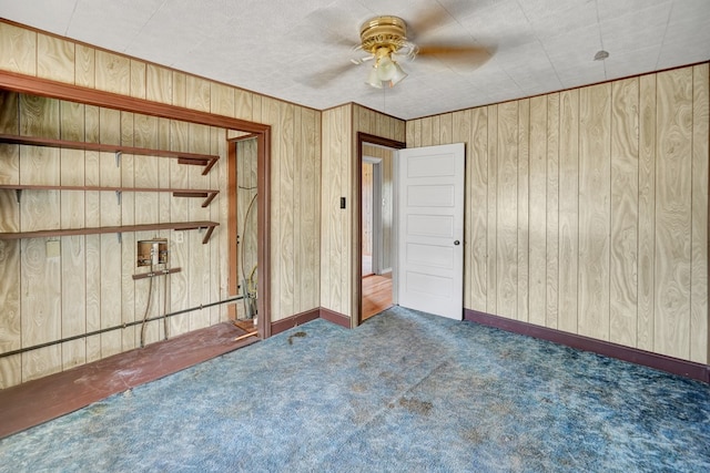 unfurnished bedroom with carpet, wooden walls, baseboards, and a ceiling fan