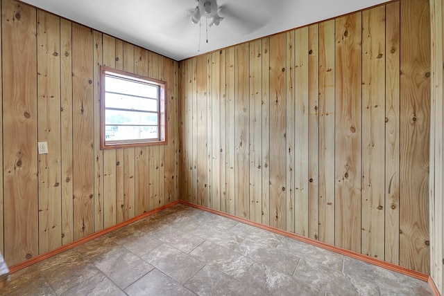 empty room with a ceiling fan, wood walls, baseboards, and stone finish flooring